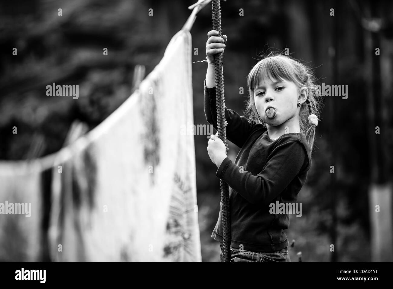 Ragazza divertente con la stendibiancheria, guarda nella macchina fotografica e mostra la lingua. Fotografia in bianco e nero. Foto Stock