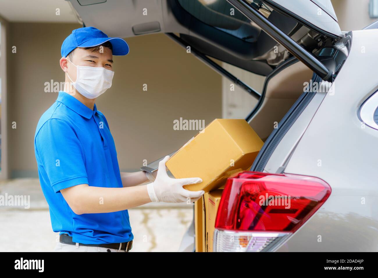 Asian Delivery uomo servizi corriere lavorando con scatole di cartone su furgone durante la pandemia di Coronavirus (COVID-19), corriere che indossa maschera medica e l Foto Stock