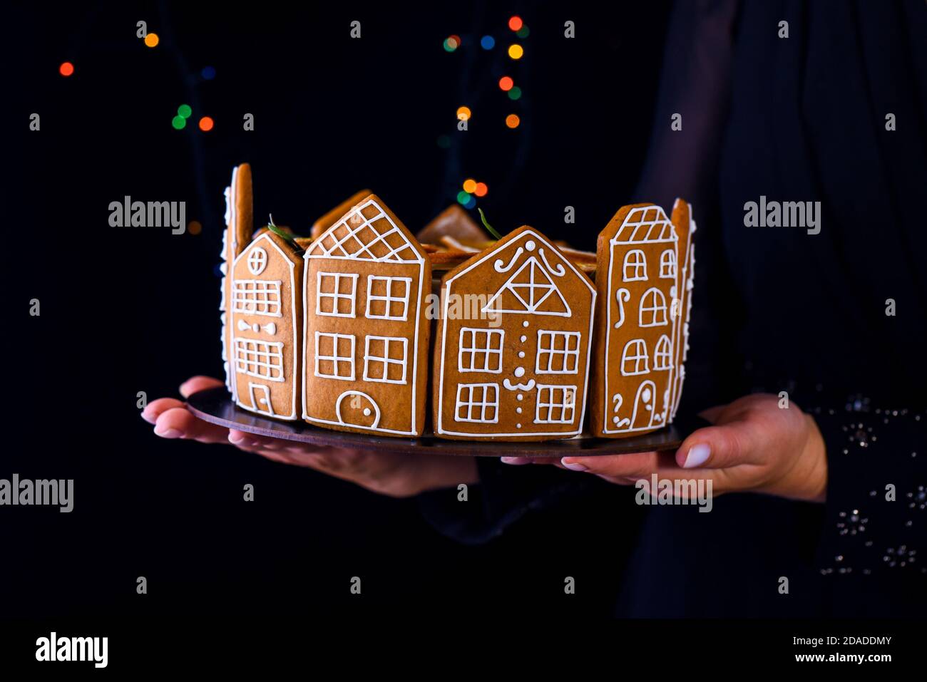 Una ragazza che tiene una torta di Natale con le case di pan di zenzero. Una torta di compleanno. Contenuti per le festività. Foto Stock