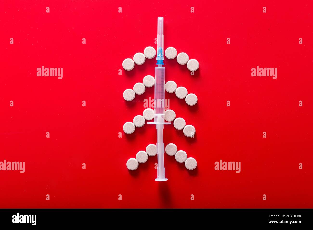 Siringa e pillole a forma di albero di Natale su sfondo rosso Foto Stock