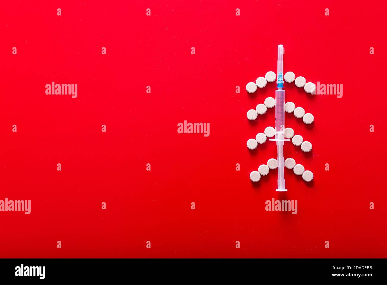 Siringa e pillole a forma di albero di Natale su sfondo rosso Foto Stock