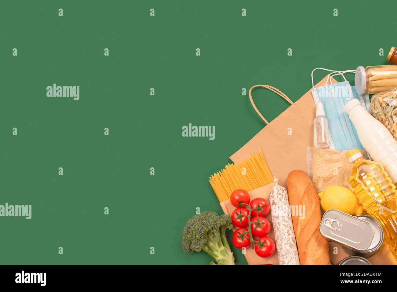 Сomposition con donazioni di cibo e medicine su sfondo verde con copyspace - pasta, verdure fresche, cibo in scatola, baguette, olio da cucina. Cibo Foto Stock