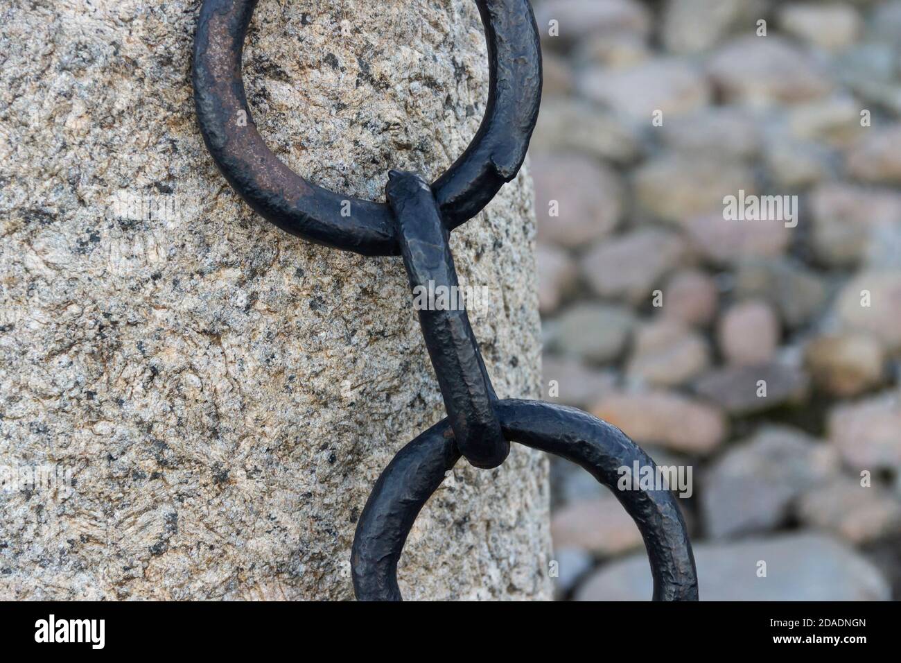 Vecchia catena arrugginita forgiata con vernice che si spellano sullo sfondo delle pietre di pavimentazione. Foto Stock