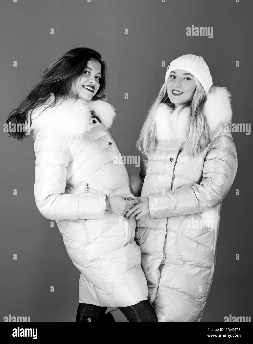 Amici di moda. Stagione invernale. Pelliccia morbida. Per coloro che  desiderano soggiornare moderno. Vestiti invernali. Le donne indossano  giacca piumino con cappuccio in pelliccia. Ragazze sorridenti trucco volti  indossare giacche invernali sfondo