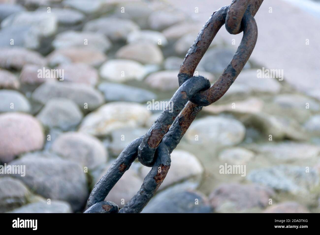 Vecchia catena arrugginita forgiata con vernice che si spellano sullo sfondo delle pietre di pavimentazione. Foto Stock