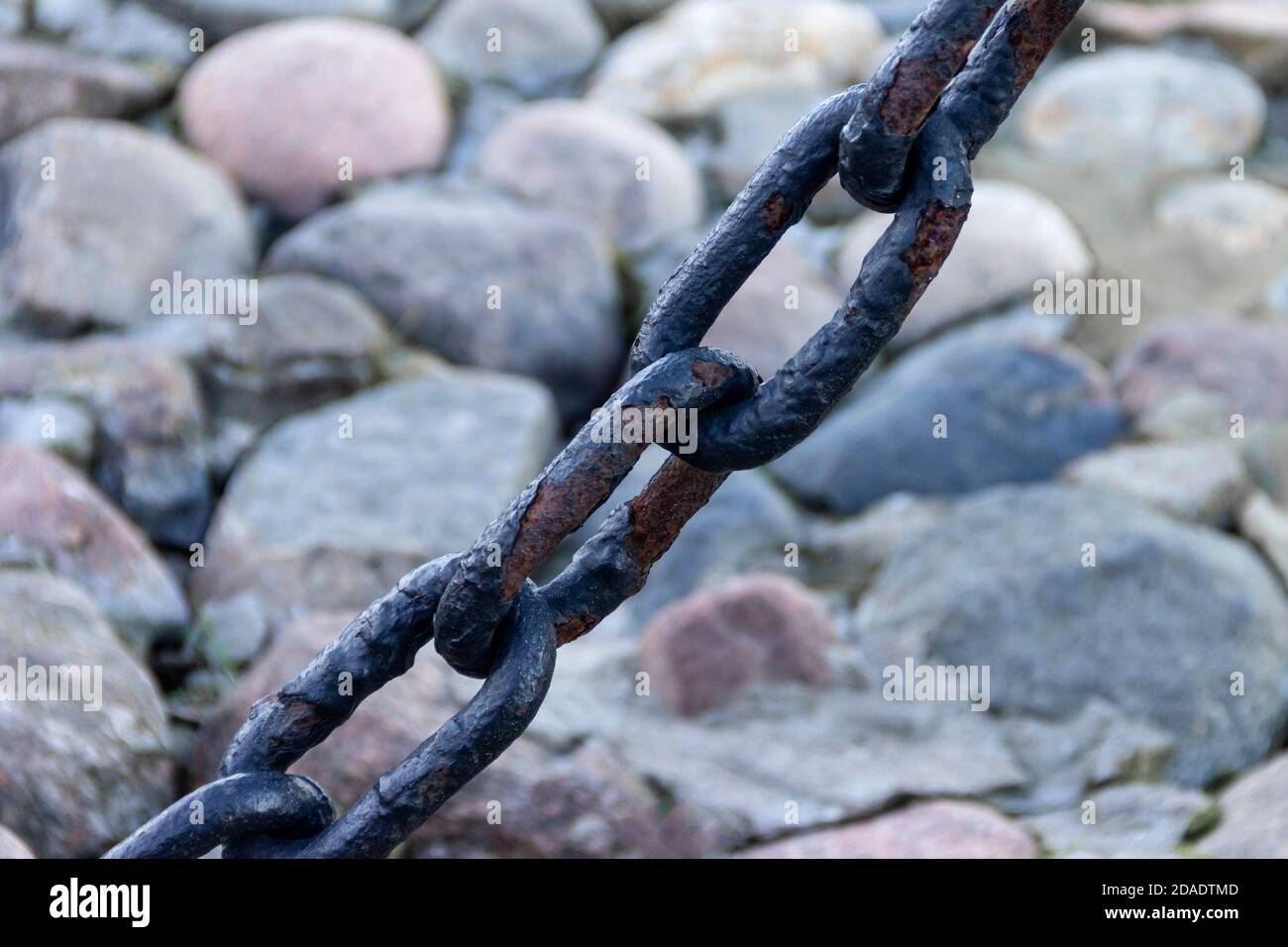 Vecchia catena arrugginita forgiata con vernice che si spellano sullo sfondo delle pietre di pavimentazione. Foto Stock