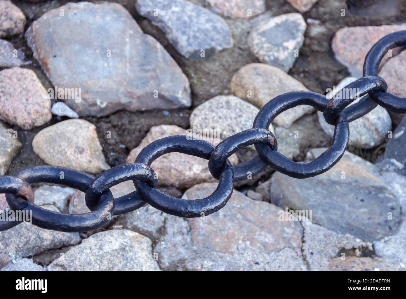 Vecchia catena arrugginita forgiata con vernice che si spellano sullo sfondo delle pietre di pavimentazione. Foto Stock
