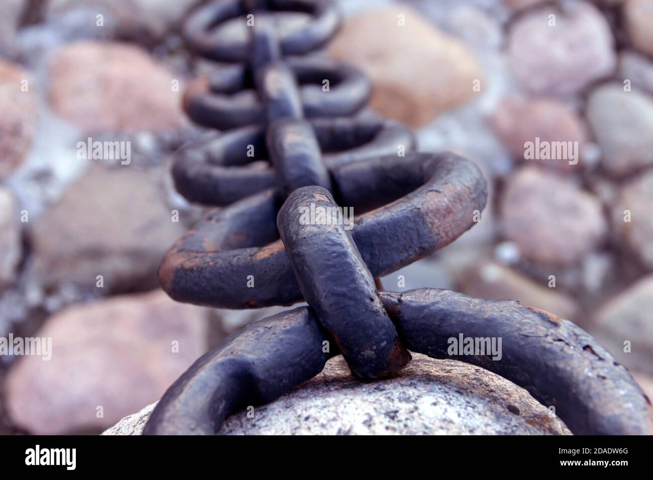 Vecchia catena arrugginita forgiata con vernice che si spellano sullo sfondo delle pietre di pavimentazione. Foto Stock