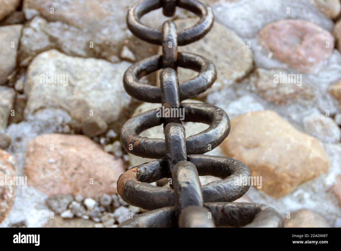 Vecchia catena arrugginita forgiata con vernice che si spellano sullo sfondo delle pietre di pavimentazione. Foto Stock