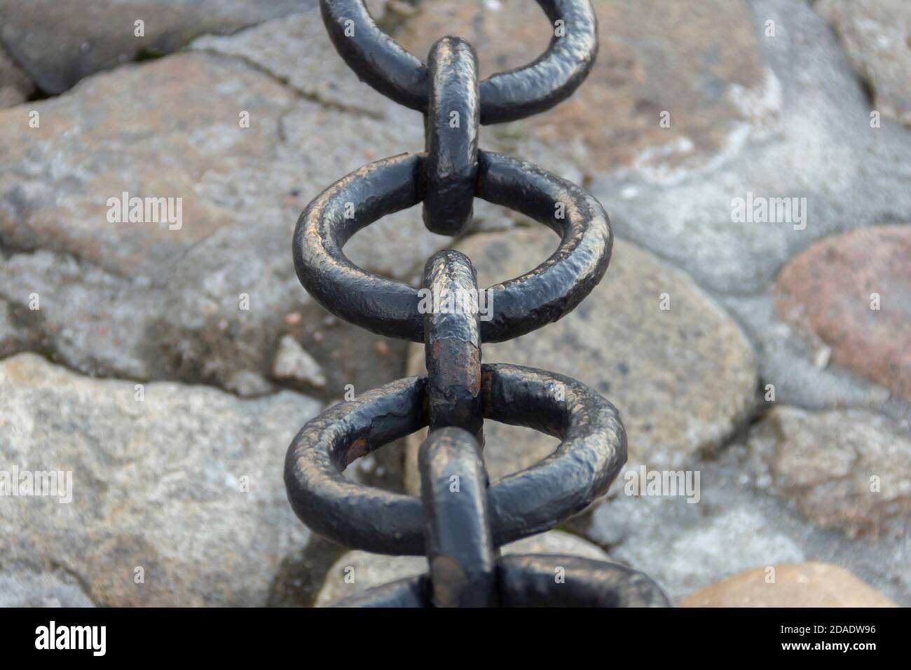 Vecchia catena arrugginita forgiata con vernice che si spellano sullo sfondo delle pietre di pavimentazione. Foto Stock