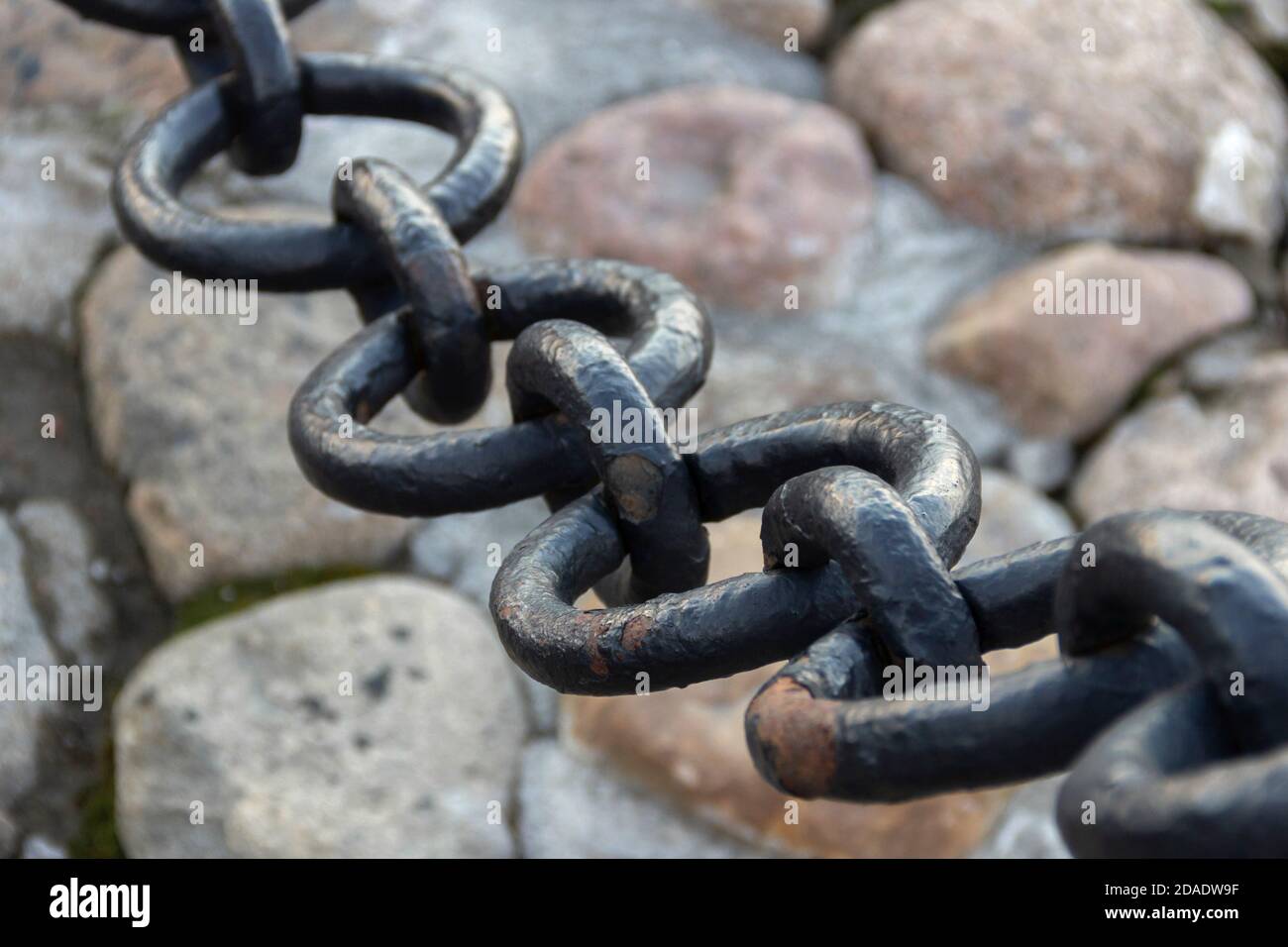 Vecchia catena arrugginita forgiata con vernice che si spellano sullo sfondo delle pietre di pavimentazione. Foto Stock