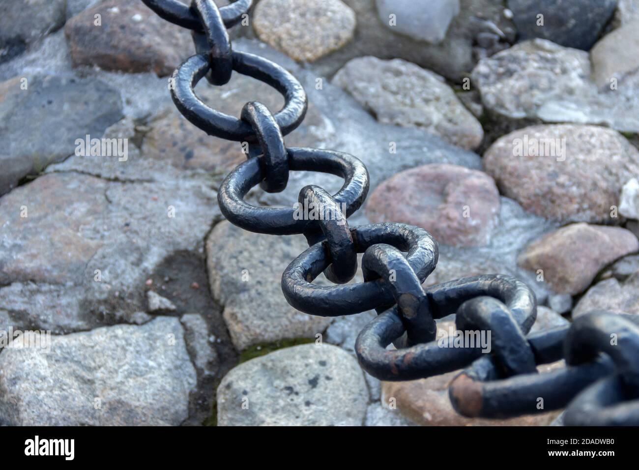 Vecchia catena arrugginita forgiata con vernice che si spellano sullo sfondo delle pietre di pavimentazione. Foto Stock