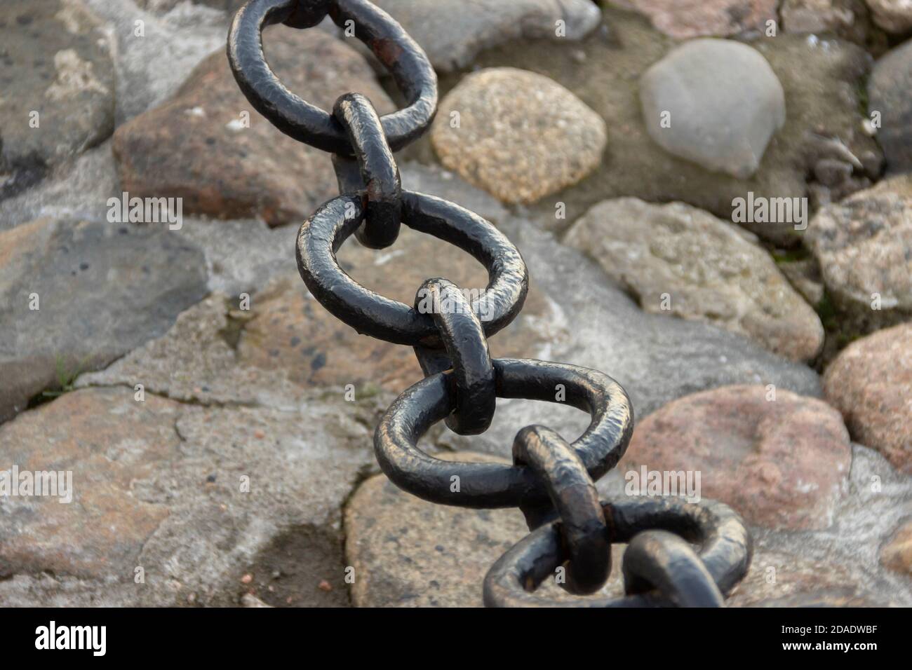 Vecchia catena arrugginita forgiata con vernice che si spellano sullo sfondo delle pietre di pavimentazione. Foto Stock