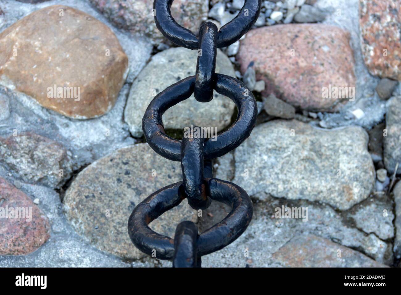 Vecchia catena arrugginita forgiata con vernice che si spellano sullo sfondo delle pietre di pavimentazione. Foto Stock