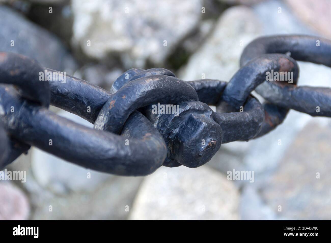 Vecchia catena arrugginita forgiata con vernice che si spellano sullo sfondo delle pietre di pavimentazione. Foto Stock