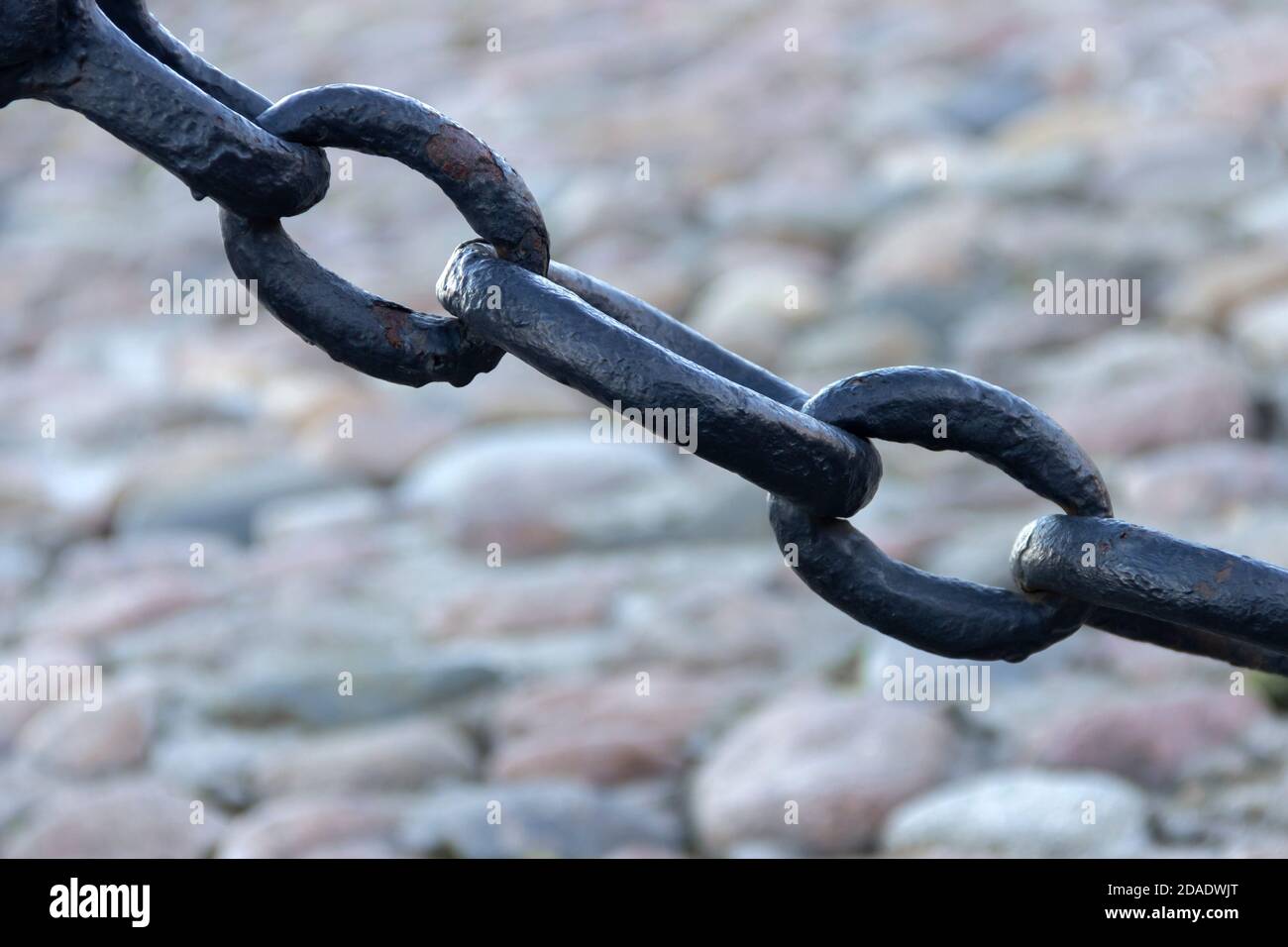 Vecchia catena arrugginita forgiata con vernice che si spellano sullo sfondo delle pietre di pavimentazione. Foto Stock