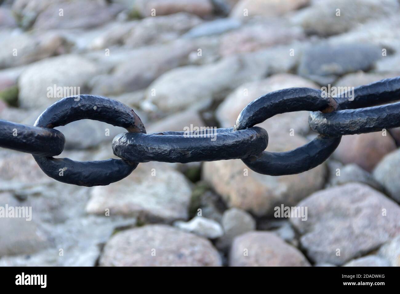 Vecchia catena arrugginita forgiata con vernice che si spellano sullo sfondo delle pietre di pavimentazione. Foto Stock