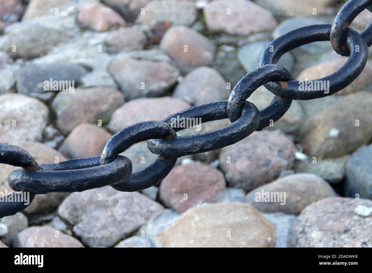 Vecchia catena arrugginita forgiata con vernice che si spellano sullo sfondo delle pietre di pavimentazione. Foto Stock