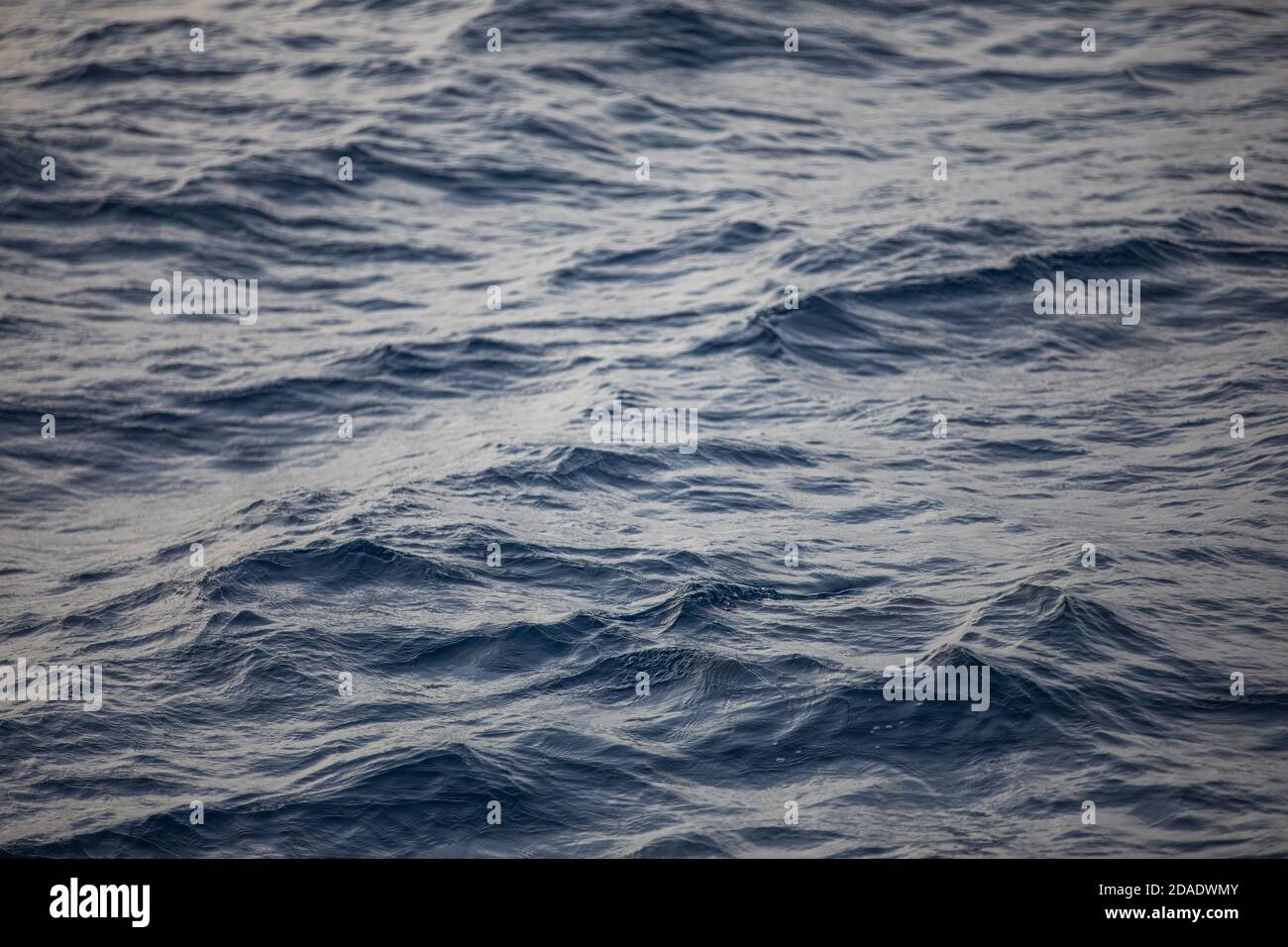 Superficie blu del mare con onde luminose. Trama di fondo di un oceano azzurro calmo e profondo con increspature sulla superficie dell'acqua di mare Foto Stock