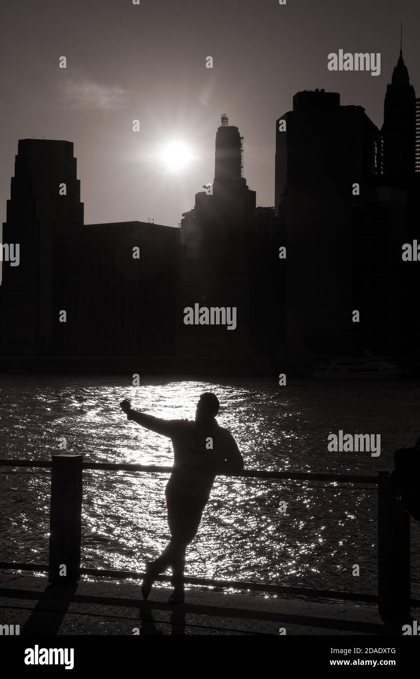 Silhouette di un giovane uomo che prende un selfie sul Sfondo del fiume est e il sole che tramonta con I grattacieli di Manhattan a New York Foto Stock