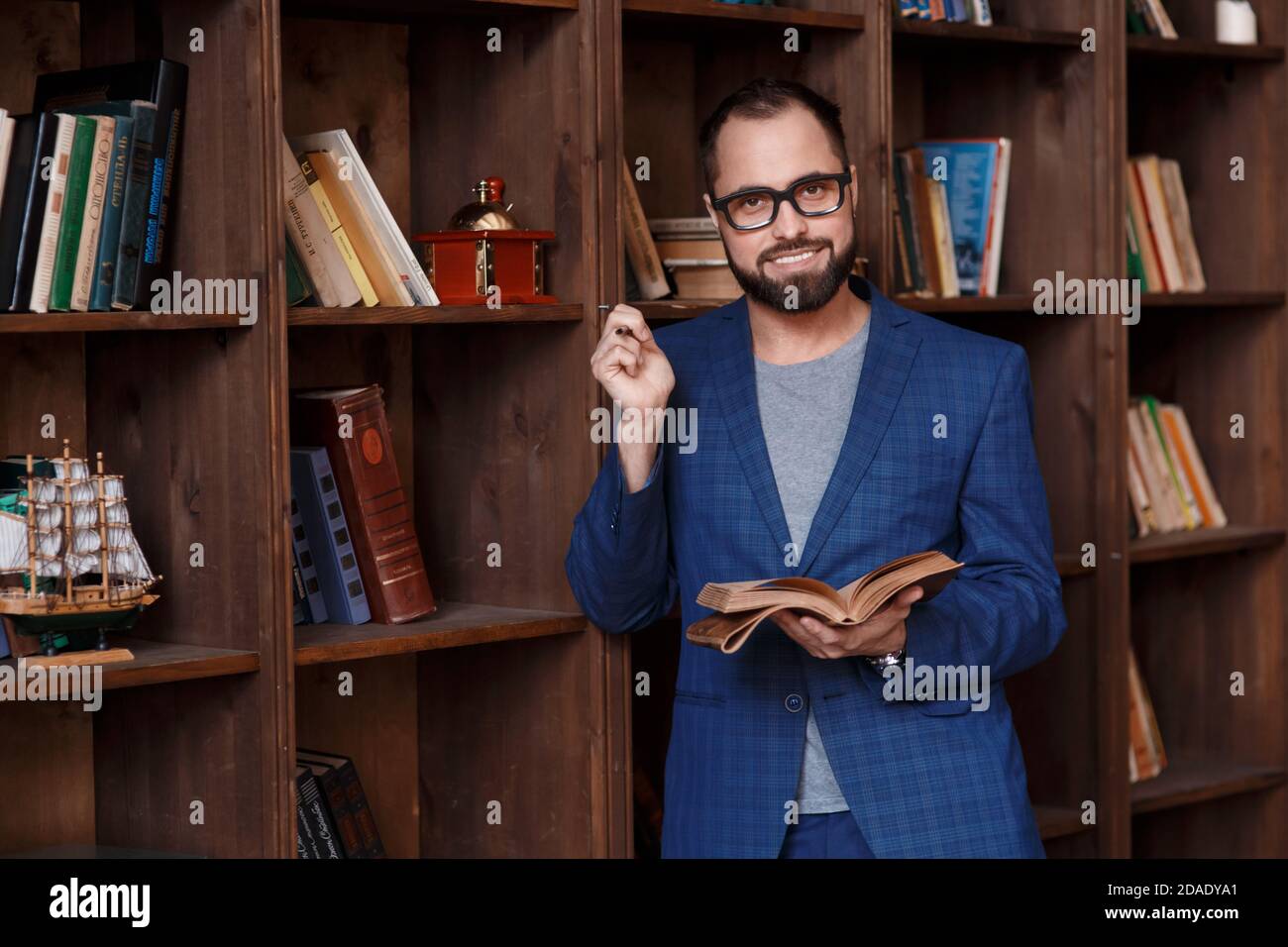 uomo d'affari bearded con gli occhiali in biblioteca con un taccuino in mano sorride. Giovane scrittore Foto Stock