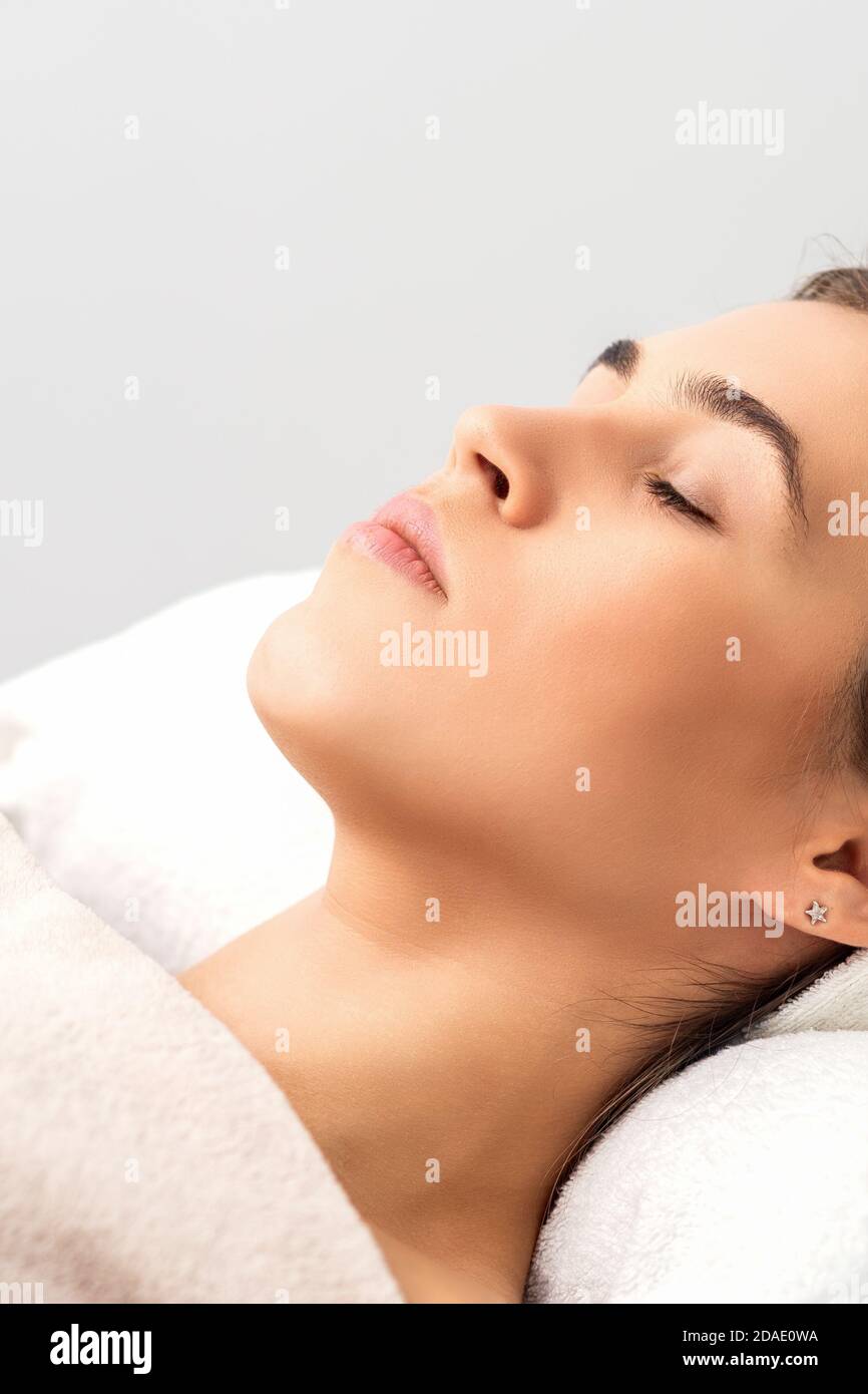 Vista laterale di giovane donna sdraiata su tavolo estetista con occhi chiusi in attesa di una procedura cosmetica in salone di bellezza Foto Stock