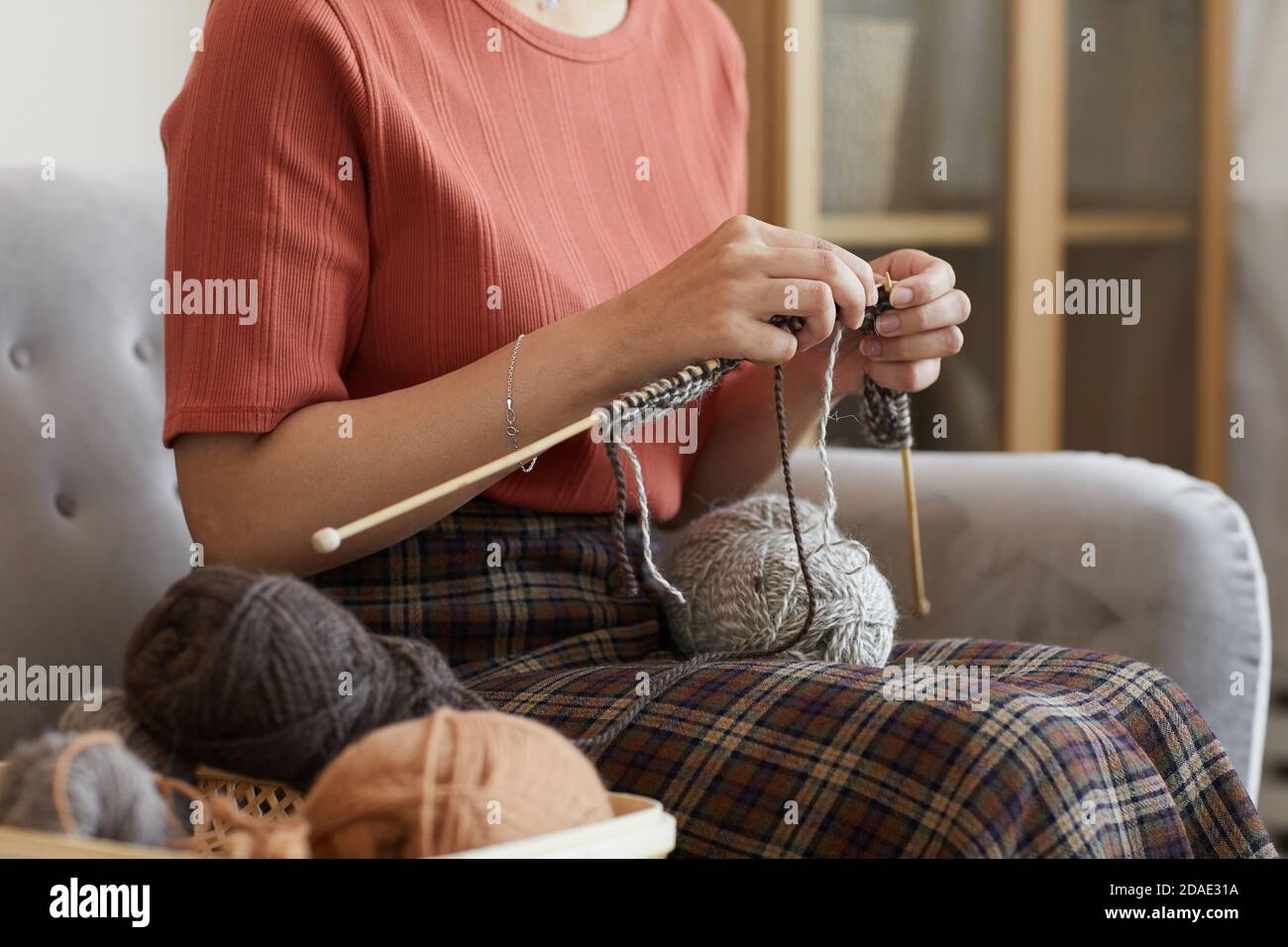 Primo piano di donna seduta sul divano e a maglia il caldo abbigliamento in camera a casa Foto Stock