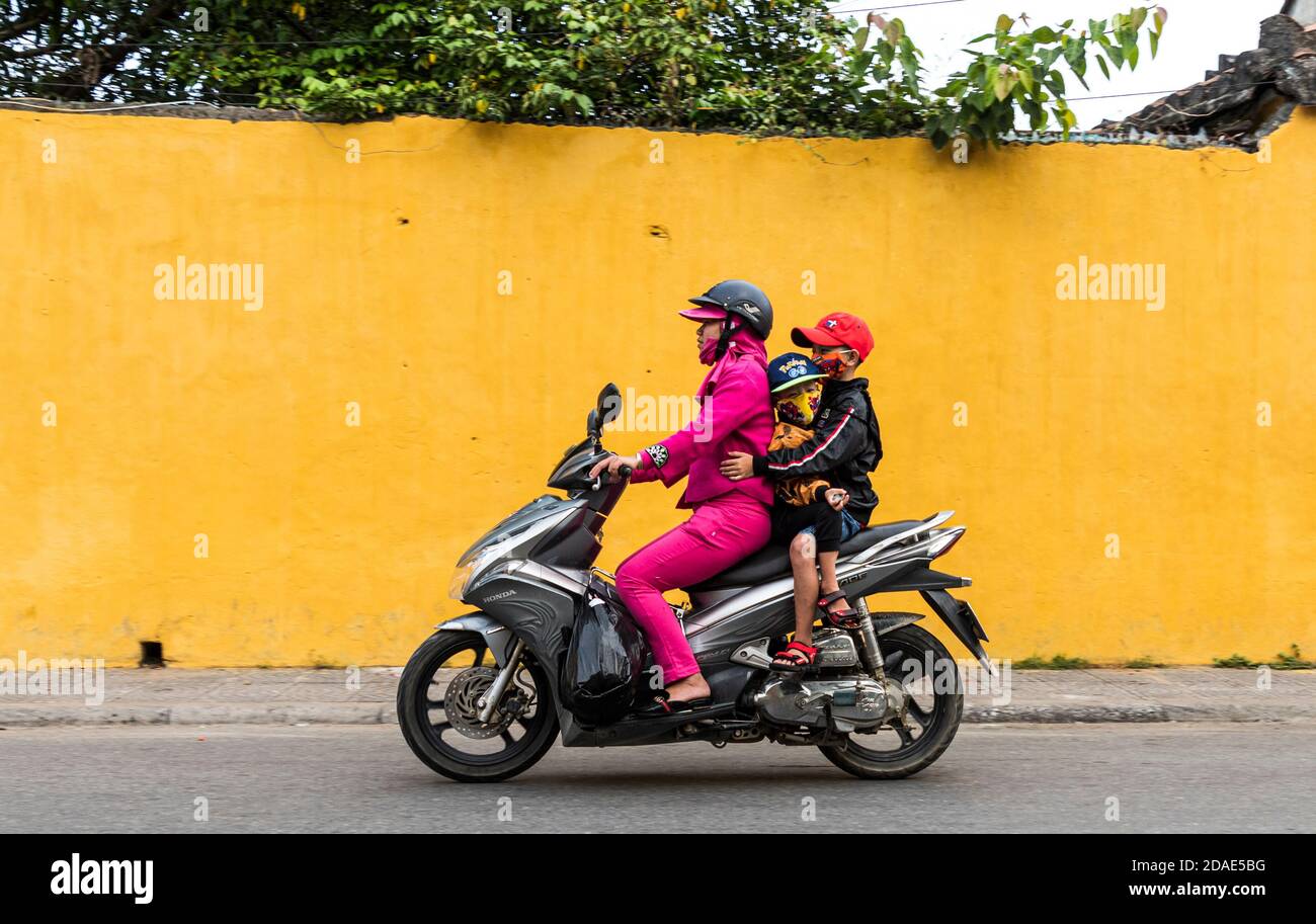 Hoi An Ancient Town, Vietnam, 27 gennaio 2020 - Donna in sella a uno scooter con casco e i suoi figli, come passeggero, senza casco in una strada a Hoi Foto Stock