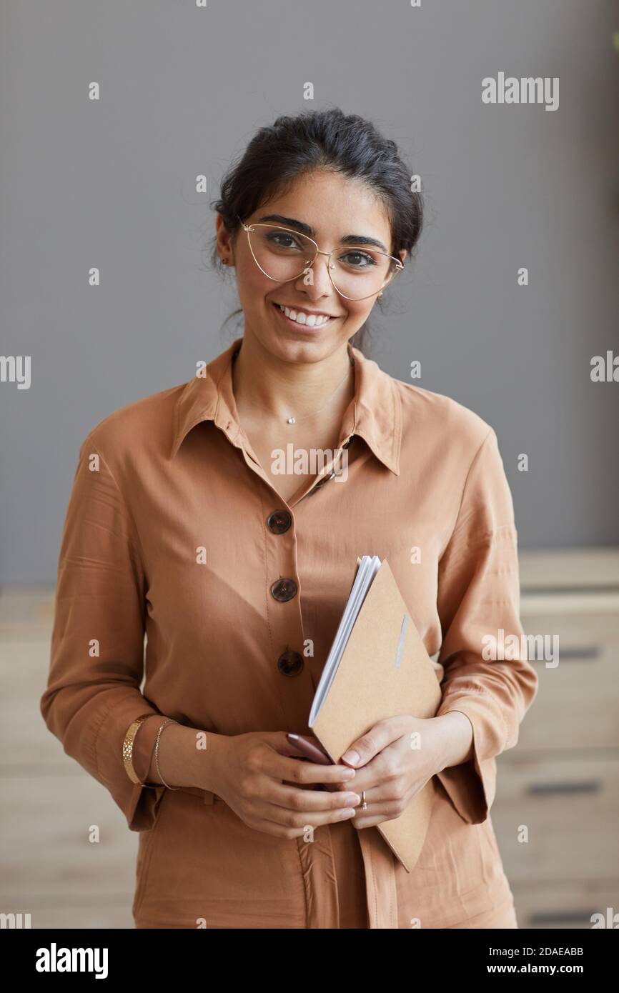Ritratto di giovane donna d'affari riuscita in occhiali sorridenti a macchina fotografica mentre si è in ufficio Foto Stock