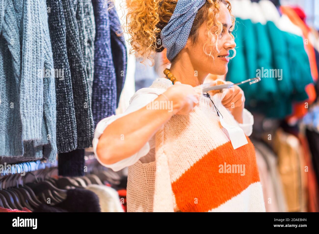 Felice donna che prova e indossa un nuovo maglione per la stagione invernale in un negozio - concetto di shopping e vendite - la gente acquista giacche colorate Foto Stock