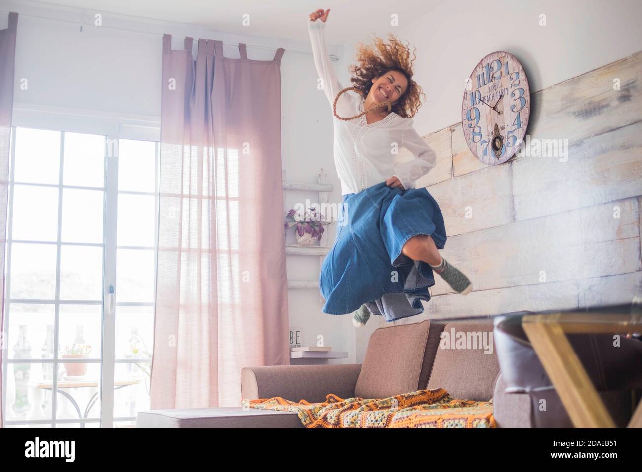 Stile di vita gioioso e concetto di successo per le donne - donna saltando sul divano per la felicità - allegro positivo giovane caucasica signora godere la nuova vita con un salto Foto Stock