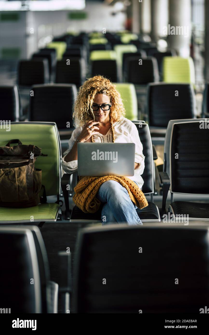Donna adulta sola aspetta al cancello dell'aeroporto per lei volo - concetto di nomade digitale e connessione internet - ritardo e cancellazione dei diritti di viaggio per il turista e il lavoratore Foto Stock