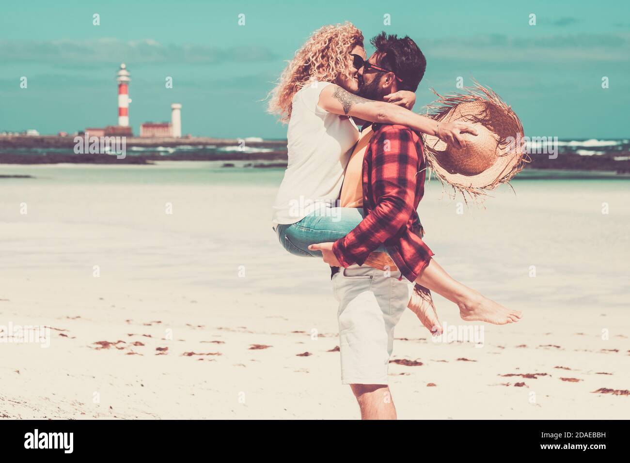 carino coppia di persone baciarsi l'un l'altro avendo divertimento e. godendo insieme alla spiaggia sulla sabbia in vacanza - due adulti innamorati in vacanze estive - uomo che tiene portando la moglie e baciandola Foto Stock