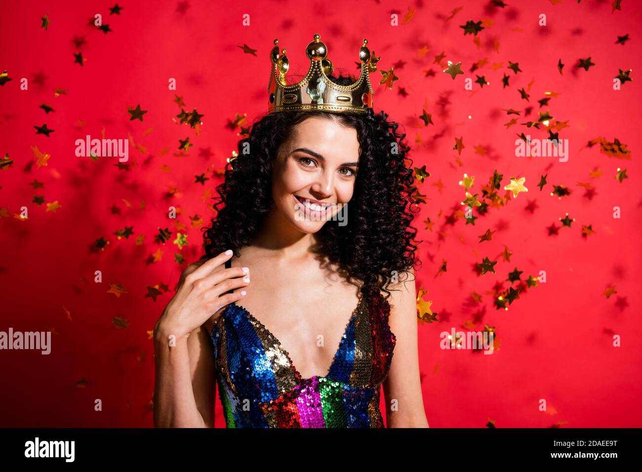 Foto di tenera stella della ragazza che si insuadono sul petto di palma sorridente indossa una corona dorata lucida abito incandescente isolato colore rosso vibrante sfondo Foto Stock