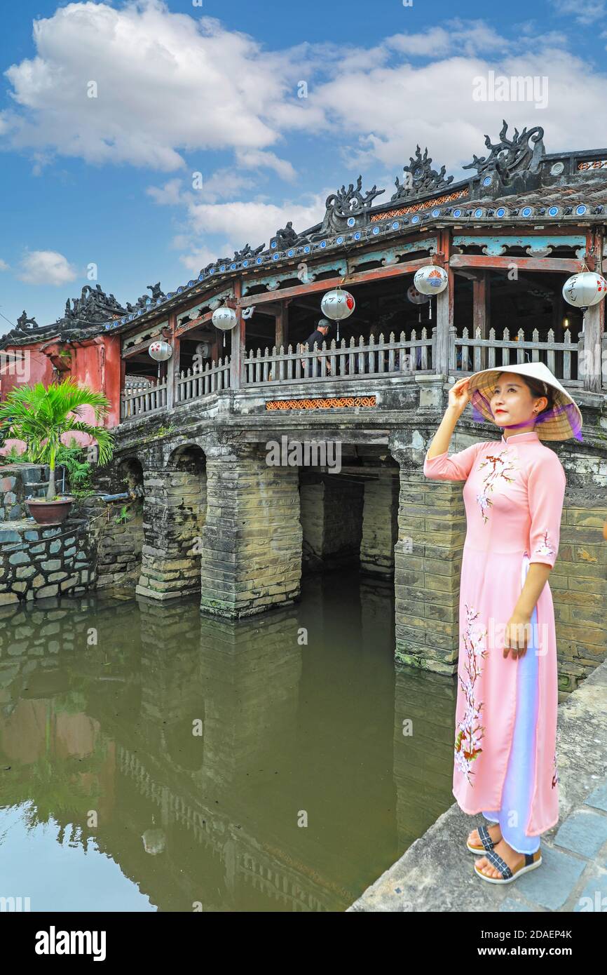 Una giovane donna vietnamita in abito tradizionale, l'ao dai, in posa per una fotografia al ponte coperto giapponese, Hoi An, Vietnam, Asia Foto Stock