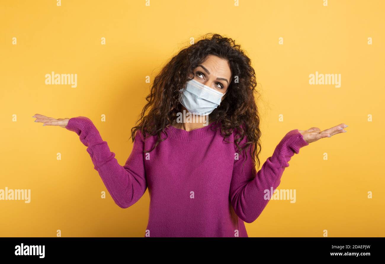 Ragazza con maschera facciale ha un sacco di domanda su covid 19. Sfondo giallo Foto Stock