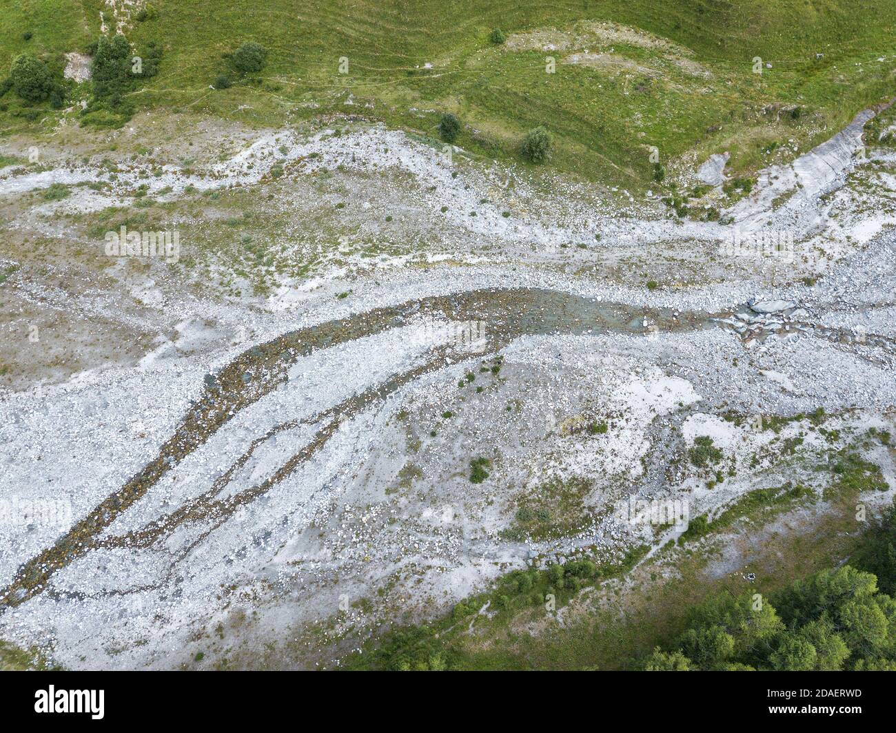 Letto di fiume sassoso in alta stagione estiva circondato da verde prateria alpina Foto Stock
