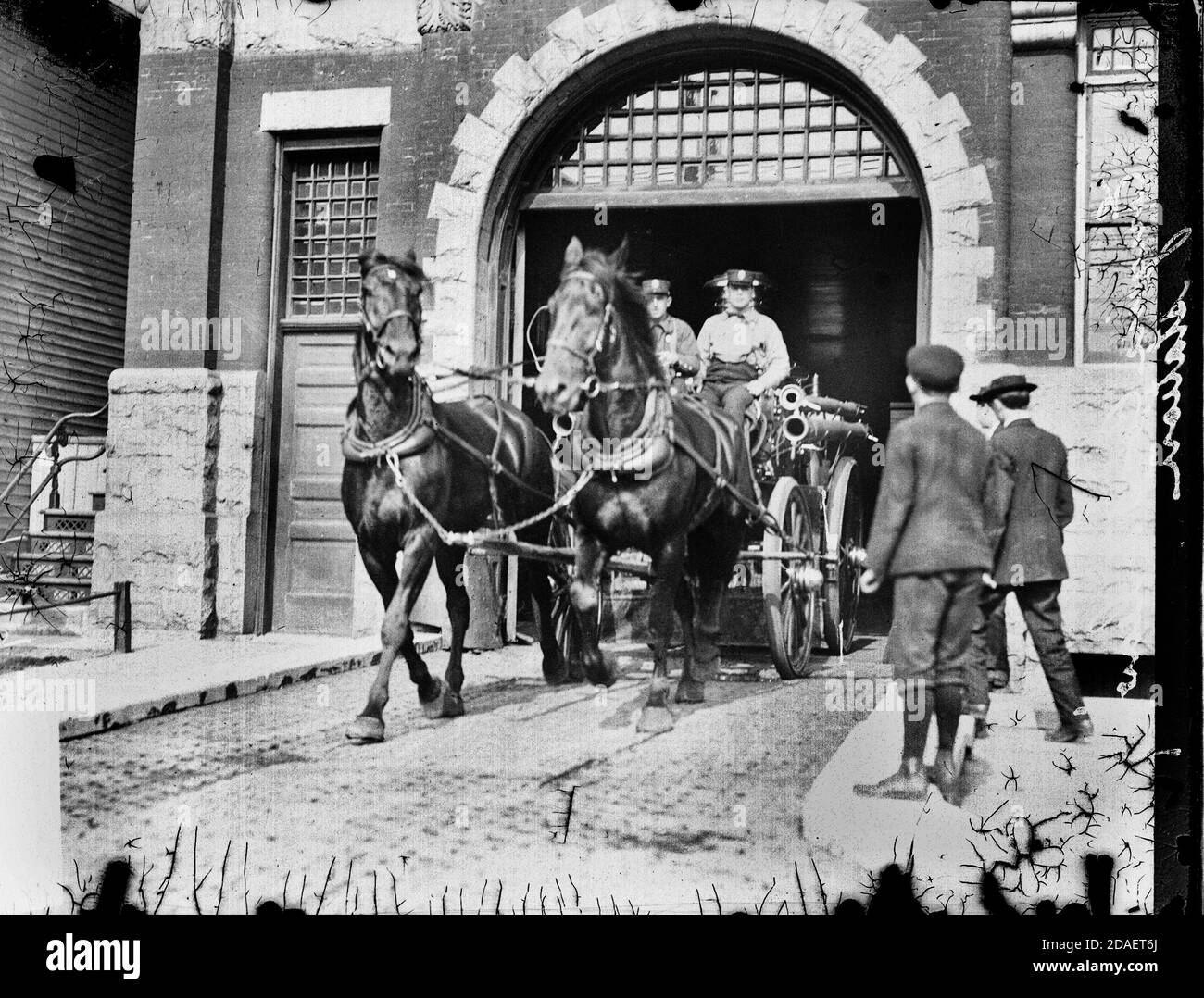 Immagine di pompieri che guidano un motore a fuoco trainato da cavalli fuori da una stazione mentre due ragazzi guardano dal lato del vialetto di Chicago, Illinois. Foto Stock