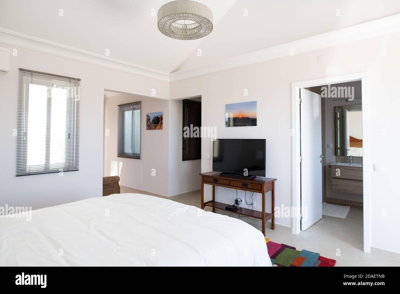 Camera da letto principale con biancheria bianca, tv sul tavolo laterale e porta al bagno interno Foto Stock