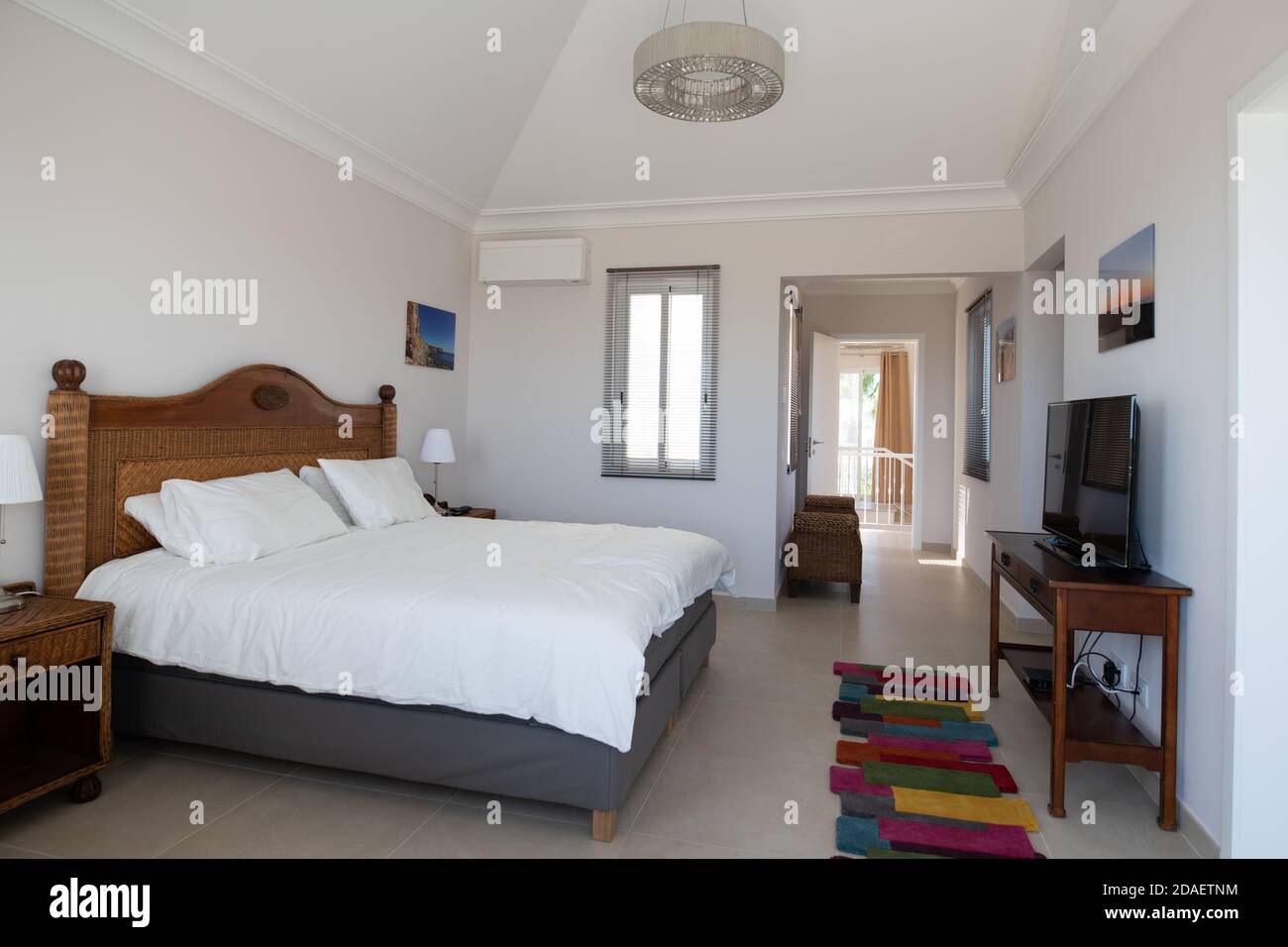 Camera da letto principale con mobili in legno e biancheria da letto bianca in una camera luminosa e ariosa in una villa per vacanze ristrutturata Foto Stock