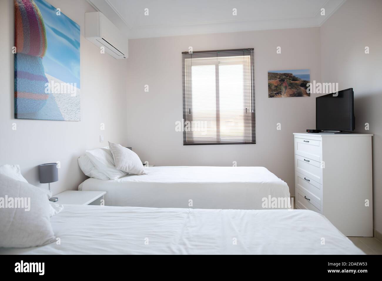 Camera doppia pulita in una casa con biancheria da letto bianca E pareti bianche e cabinet con TV Foto Stock