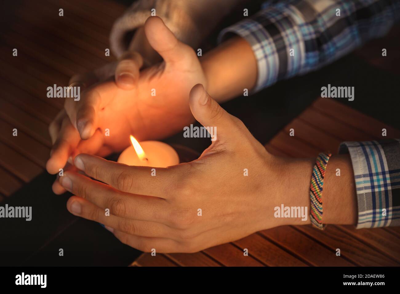 Primo piano delle mani della coppia si sono accucchiate intorno ad una candela bruciante. Mani di giovane uomo e donna che proteggono la fiamma di una candela. Concetto di storia d'amore Foto Stock