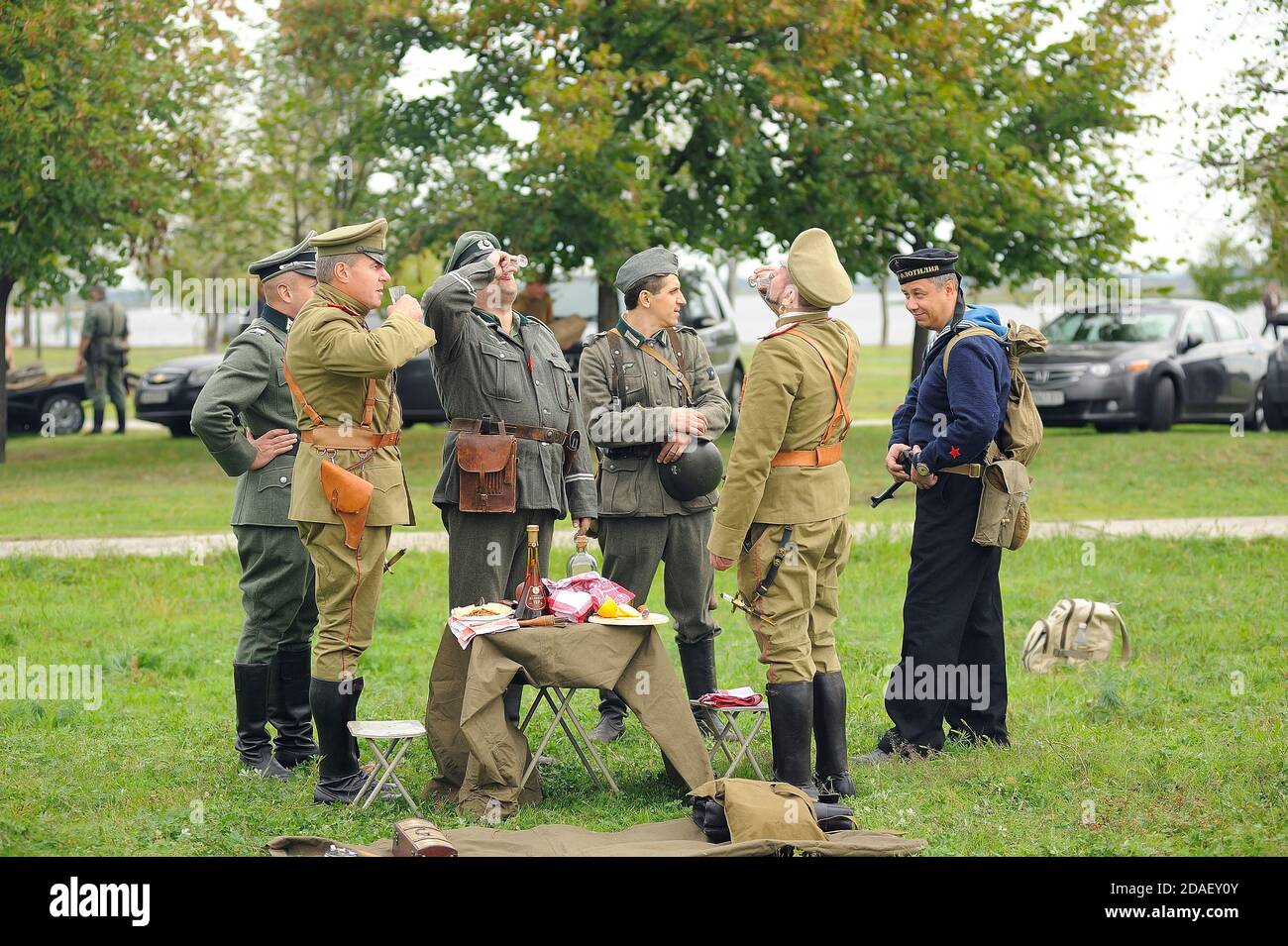 I reenattori vestiti in uniformi di ufficiali tedeschi della seconda guerra mondiale e ufficiali russi della prima guerra mondiale che bevono vodka su un prato. 4 ottobre 2012. Kiev, Foto Stock