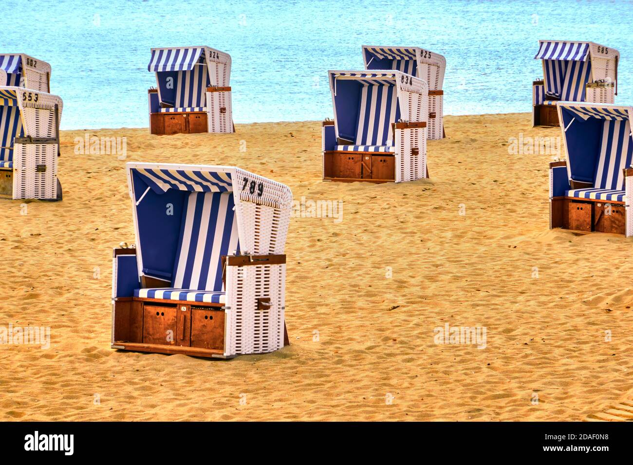 Cestelli vuoti in corda bianca con coperture a strisce blu e bianche su una spiaggia di sabbia con il mare sullo sfondo Foto Stock