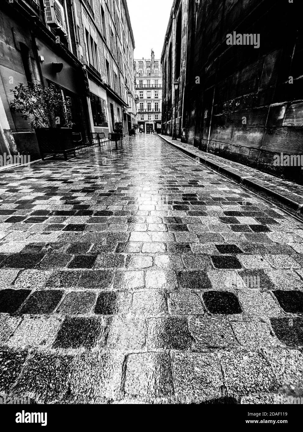 Persone irriconoscibili che camminano in una strada lastricata vuota a parigi sotto la pioggia Foto Stock