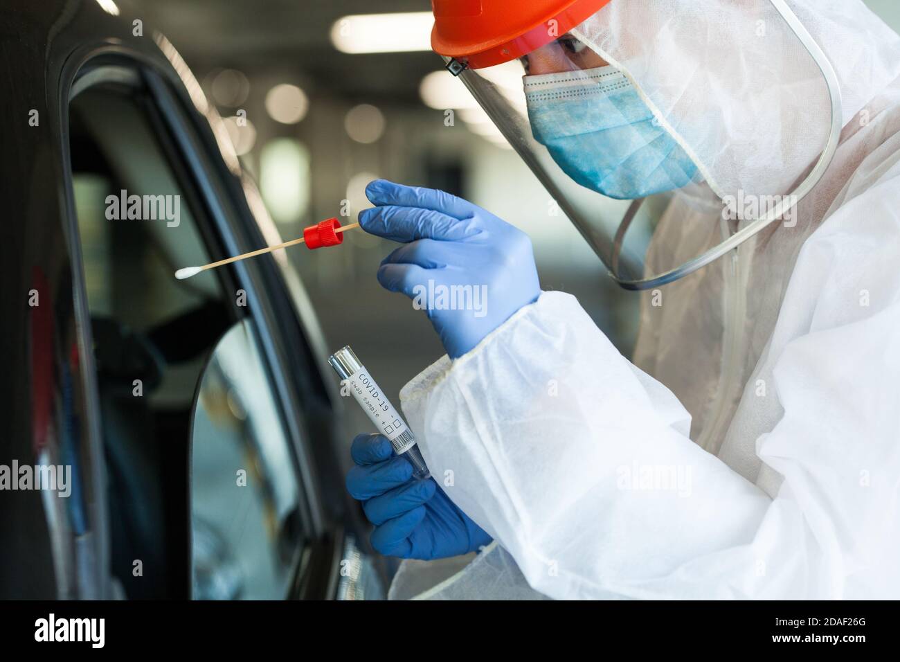 Lavoratore medico di NHS in dispositivi di protezione personale che ingerono una persona In auto guidare attraverso Coronavirus COVID-19 mobile test center, orale e nasale Foto Stock
