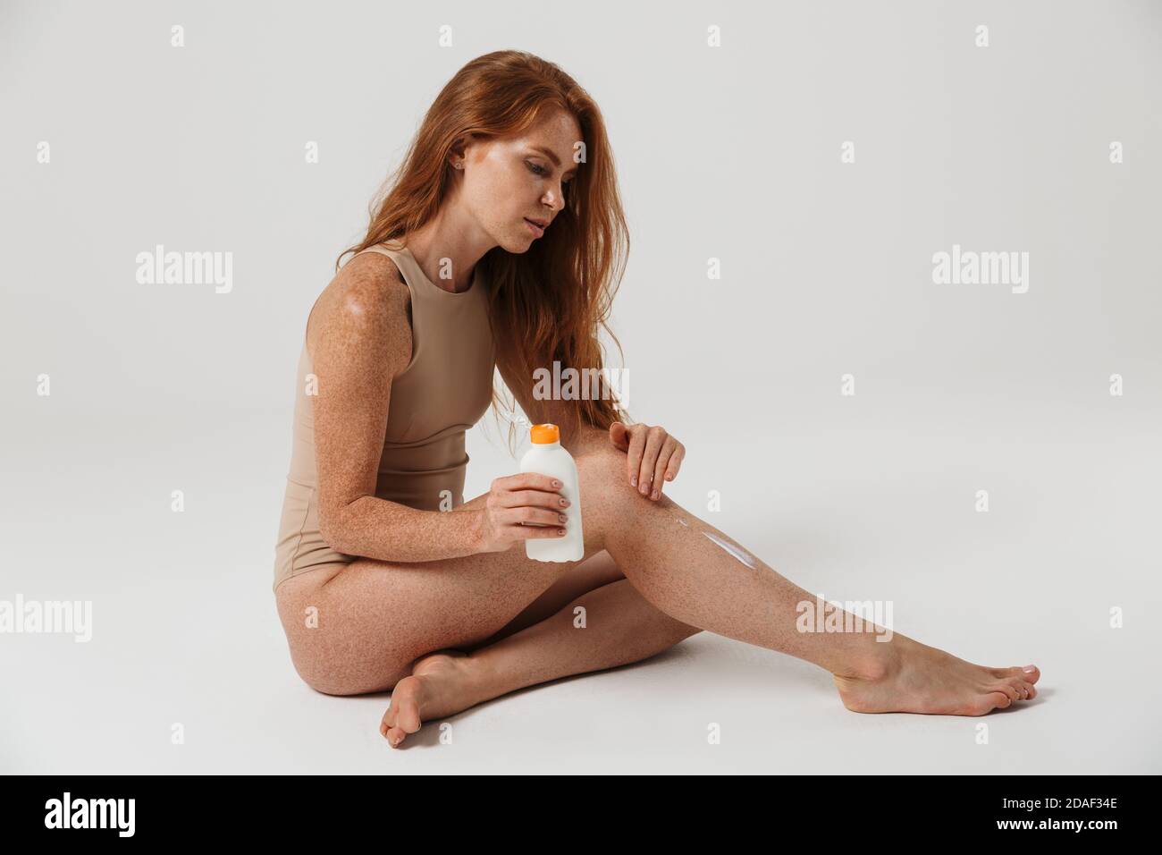 Immagine di bella donna rossa con i cocci che applicano la protezione solare lozione isolata su sfondo bianco della parete Foto Stock