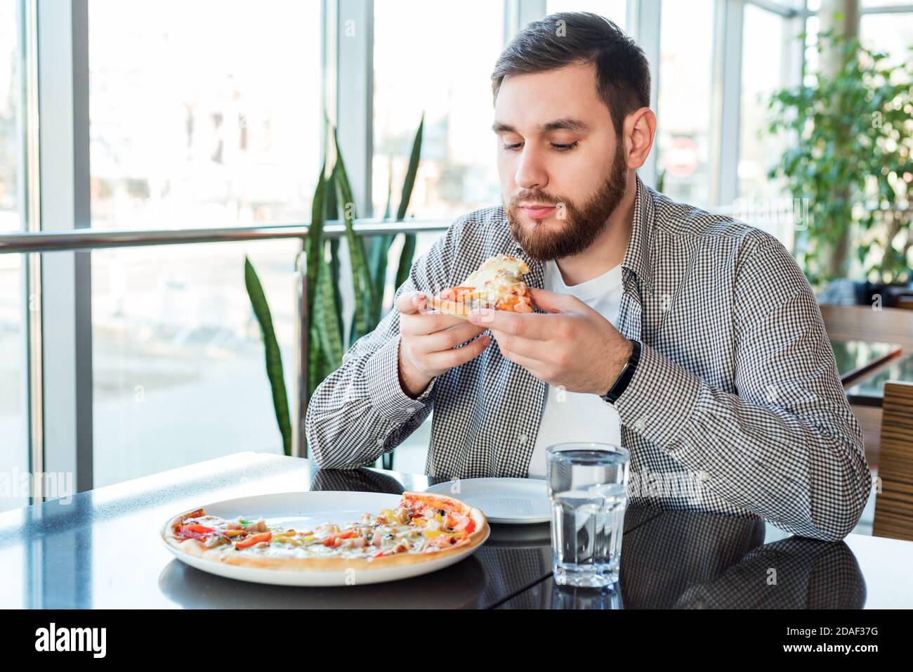 Affamato uomo caucasico mangiare pizza italiana in pizzeria. Deliziosa pizza al caffè. Foto Stock