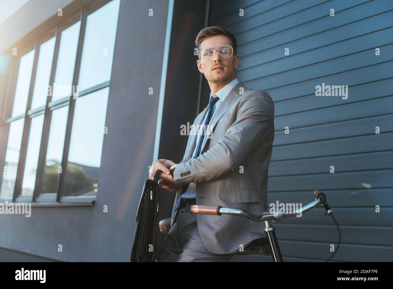 Uomo d'affari con valigia orologio da polso a contatto vicino alla bicicletta all'aperto Foto Stock