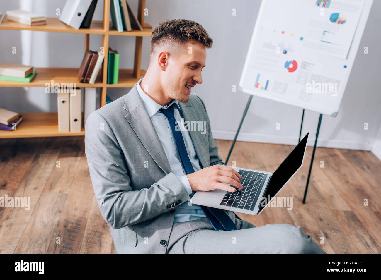Uomo d'affari allegro che usa il computer portatile mentre lavora in ufficio Foto Stock